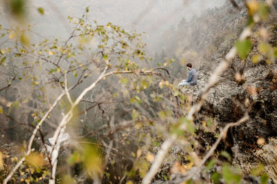 Man sitting on rocky mountain seen through trees