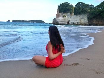 Woman performing pashchima namaskarasana while sitting at sea shore