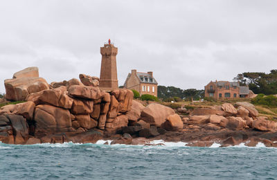 Rocks by sea against buildings in city against sky