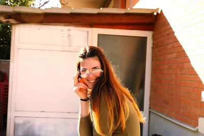 Portrait of smiling young woman using phone while standing outdoors