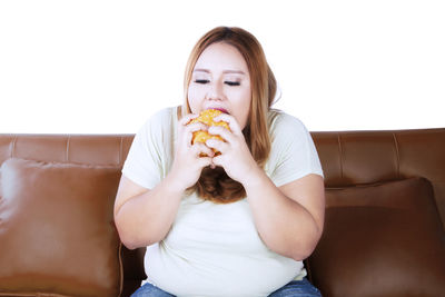 Young woman eating burger while sitting on sofa