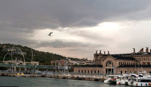 View of city at waterfront against cloudy sky