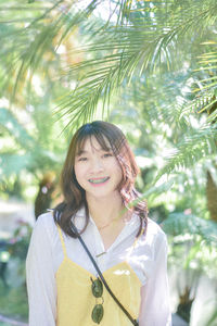 Portrait of young woman standing against trees