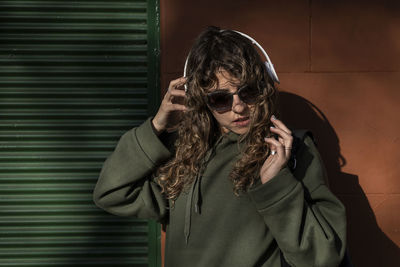 Young woman wearing sunglasses while standing against wall