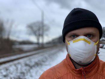 Portrait of man wearing mask standing on railroad track during winter