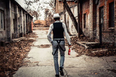 Rear view of a man holding beer bottle while walking through town street.