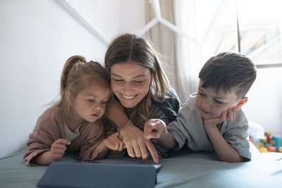 Smiling young mother with children using tablet pc in bedroom at home
