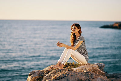 Woman sitting on rock by sea against sky