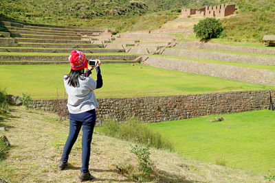 Female taking photos of the ancient stepped agricultural terraces of tipon, cusco region, peru