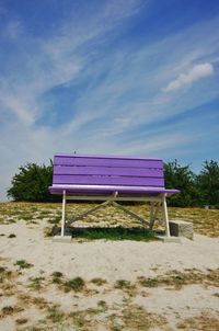 Empty bench on field against sky