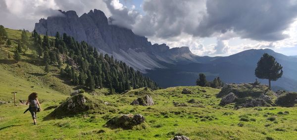 Rear view of woman walking on grass against mountains and sky