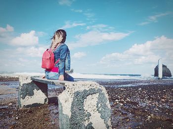 Rear view of woman sitting at sea against sky