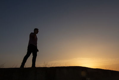 Silhouette man standing on street against sky during sunset