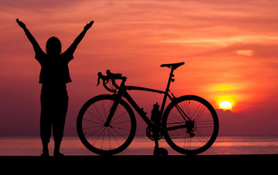 Silhouette man standing by bicycle against sky during sunset