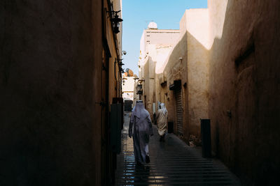 Rear view of people walking on narrow alley amidst buildings in city
