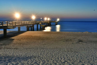 Illuminated pier over sea against sky