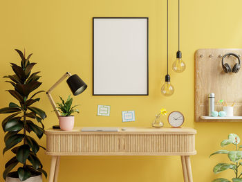 Mockup frame on work table in living room interior on empty yellow wall background.3d rendering