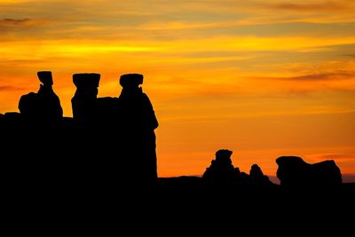 Silhouette people standing on rock against sky during sunset