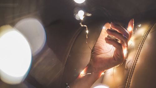 Cropped hand of woman with illuminated string lights in darkroom