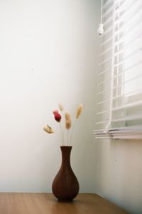 Close-up of vase on table against wall at home