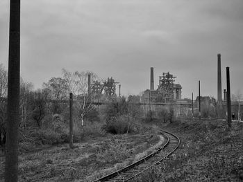 Railroad tracks by factory against sky