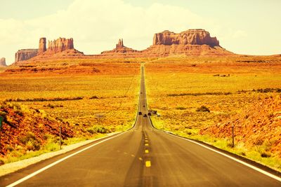 Road amidst landscape leading towards monument valley against sky