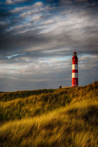 Lighthouse on field against cloudy sky