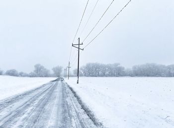 Snow covered road by electricity pylon during winter