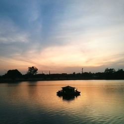 Silhouette boat sailing in calm river against cloudy sky during sunset