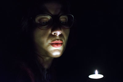 Close-up of young woman blowing candle in darkroom