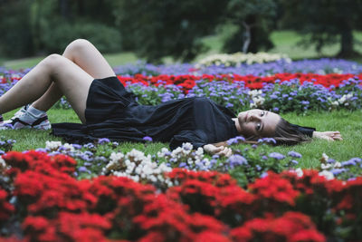 Full length of young woman lying on grass amidst flowering plants