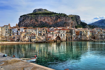 Sea by old buildings in cefalu against sky