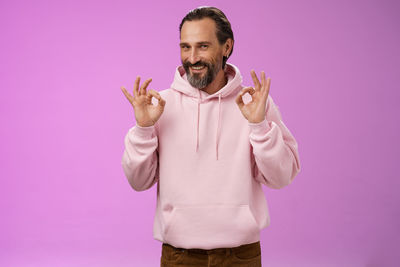 Portrait of man standing against pink background