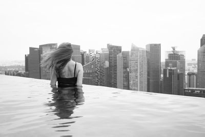 Rear view of man in swimming pool against buildings