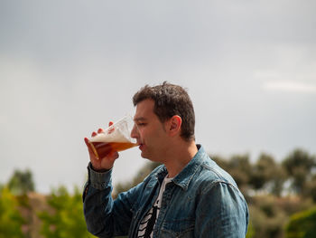 Side view of man drinking beer against sky