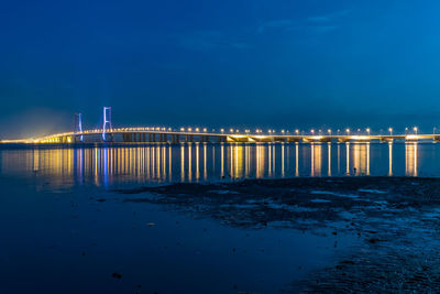Illuminated bridge over sea against sky at dusk