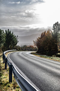 Country road by trees against sky