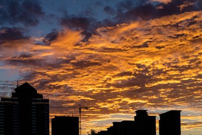 Low angle view of buildings against dramatic sky during sunset