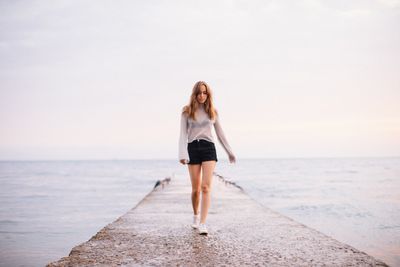 Full length of woman walking at beach against sky