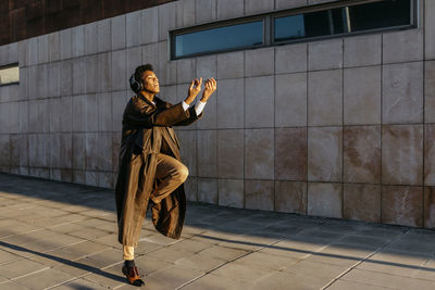 Full length of man holding umbrella on footpath against building