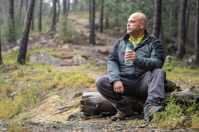 Hiker man resting on a log with a bottle of water in his hand.