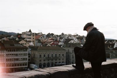 Man using phone while standing by retaining wall in city against clear sky