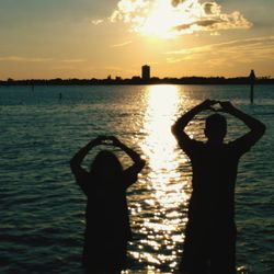 Silhouette people standing by sea against sky during sunset