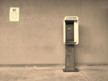 Abandoned pay phone on footpath against wall