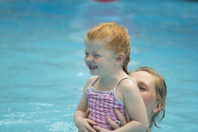 Mother holding smiling girl in swimming pool