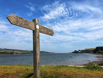 Cross on shore by lake against sky