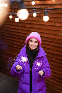 Happy young woman in outerwear with sparklers on the street on the background