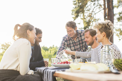 Friends having lunch at picnic table against clear sky