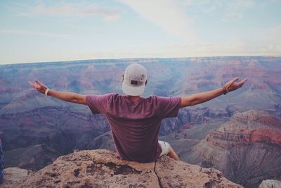 Rear view of man sitting with arms outstretched on rock at grand canyon national park