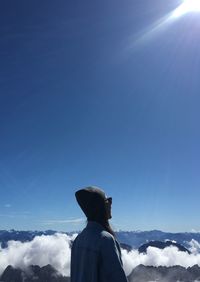 Woman looking at clouds covered mountain against blue sky during sunny day